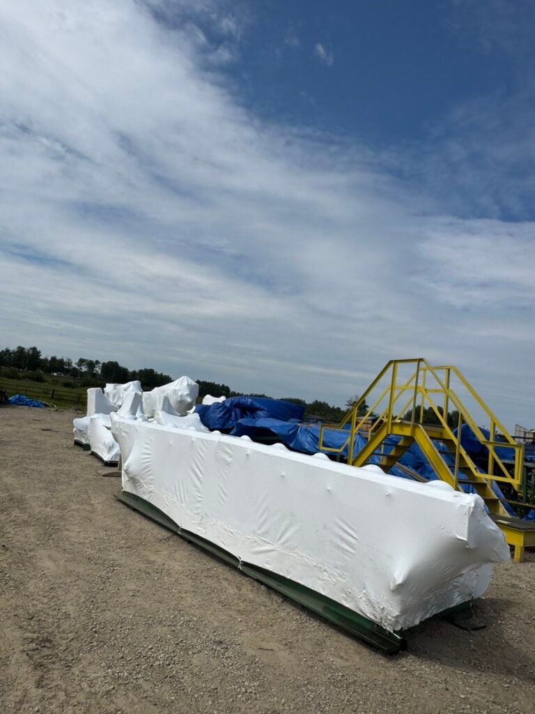 White shrink wrap protects a structural beam on a green skid.