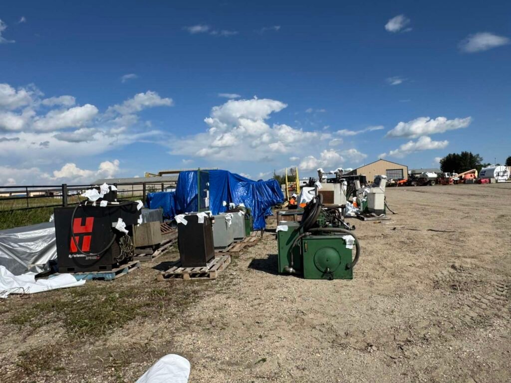 Industrial equipment in a yard includes blue-tarped and partly shrink-wrapped pieces.