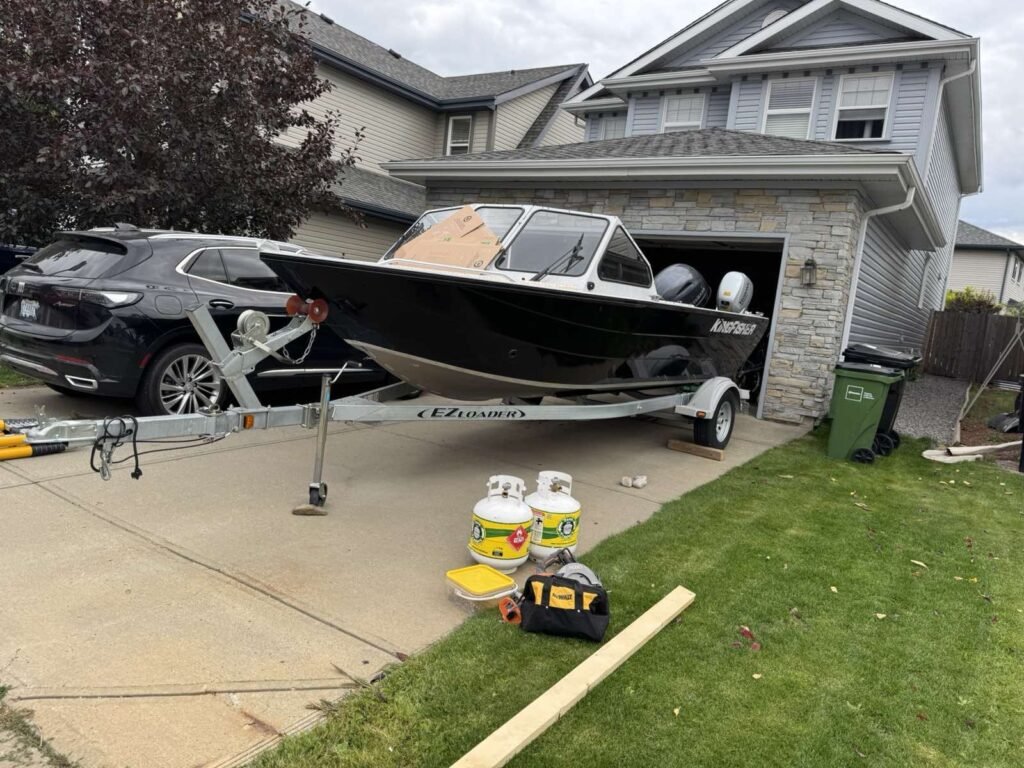 A black-and-white boat on a trailer sits uncovered in a driveway before shrink wrap.
