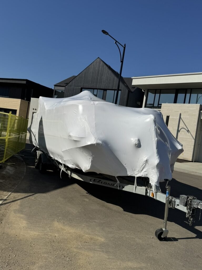 A pontoon boat on a trailer is covered in white shrink wrap.